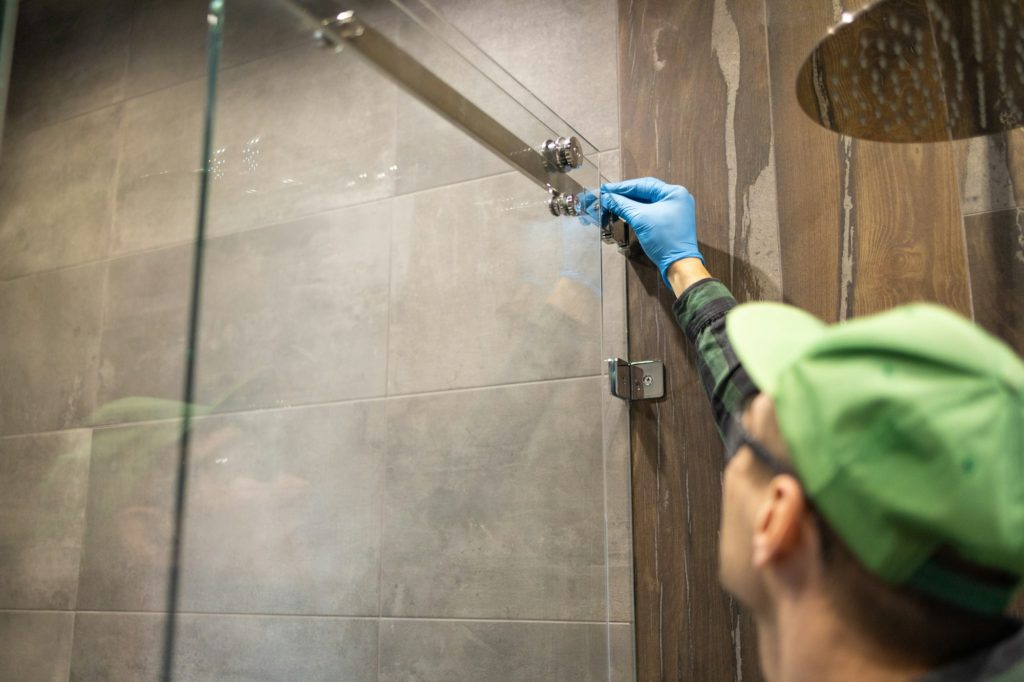 Workers are installing glass door of the shower enclosure.